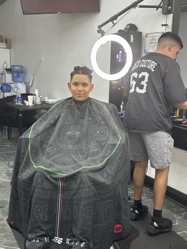 A barber cutting a client's hair under the ring light inside Extreme Cutz